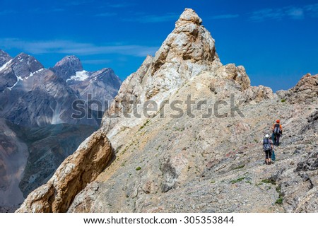 Razor sharp summit and climbers. Mountain landscape and blue sky with small bodies of people moving toward rocky summit with gear rope belaying each other