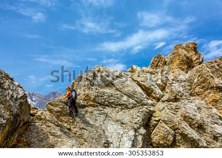 Brave man climbs rocky ridge. Male mountain climber moving on extreme sharp rock blue sky background climbing gear rope