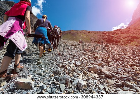 Group of People Walking Up.\
Bodies of Hikers Walking on Wild Deserted Terrain from Back Bottom Point of View Blue Sky Shining Sun and Mountain Range Background