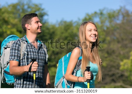Excited Travelers.\
Young Man and Woman Traveling Outdoor Expressing Fun and Pleasure with Backpacks Walking Poles Sticks and Casual Sporty Style Clothing