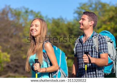 Excited Travelers.\
Young Man and Woman Traveling Outdoor Expressing Fun and Pleasure with Backpacks Walking Poles Sticks and Casual Sporty Style Clothing