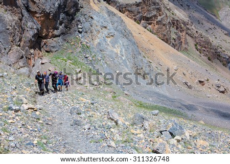 Group of Climbers Hard Walk.
Hiker Team Scramble Up on Rocky Trail with Severe Colored Steep on Background.