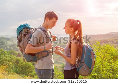 Young People Traveling and Talking.\
Girlfriend and Boyfriend Teenagers Couple with Backpacks on Green Forest Background Staying Talking Touching Smiling Joking rising Sun on Background