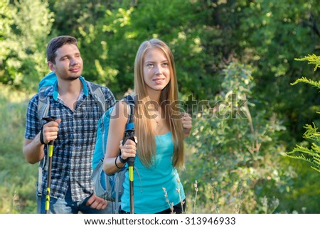 Excited Travelers Young Man and Woman Traveling Outdoor Expressing Fun and Pleasure with Backpacks Walking Poles Sticks and Casual Sporty Style Clothing on Bright Green Flora Background