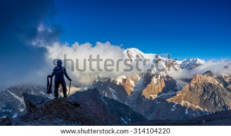 Alpine Climber Reached Summit\
Silhouette Man Staying on Top of Rock Cliff Holding Climbing Gear Stormy Clouds and Peaks Illuminated bright Morning Sun