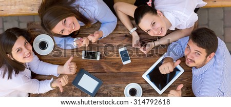 Young Happy Business People From Above Top View of Smiling Business Men At Wooden Desk Looking Smiling with Tablet Computers Telephones Coffee Mug Casual Clothing