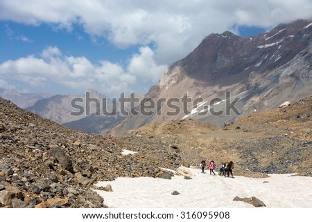 Group of Hikers Walking on Snowfield Alpine Climbers Team Sport Clothing with Heavy Backpacks and Climbing Gear Crossing Snow Place Mountain Landscape Blue Sky Clouds on Background