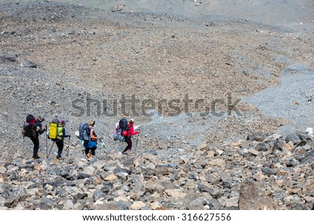Rocky mountain footpath and group of hikers.\
Mountain landscape with grey and orange color stones terrain and group of travelers walking down with backpacks and trekking poles