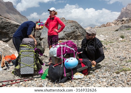 Hikers Packing Backpacks Group of People Man and Women Sitting Staying Along with Large Bags with Climbing Gear Attached such as Helmet Camping Mat Walking Poles Ice Axe