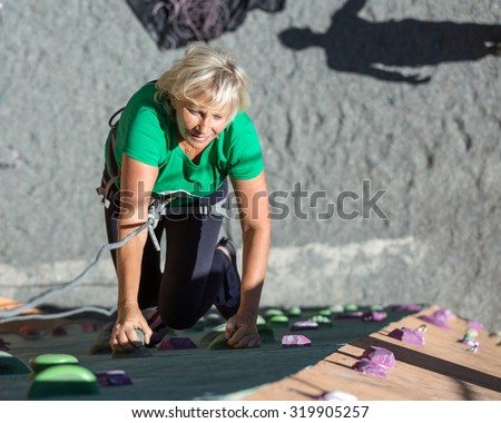 Aged Lady Doing Extreme Sport\
Elderly Female Makes Hard Move on Outdoor Climbing Wall Sporty Clothing on Fitness Training Shadow of Her Belaying Partner on Background