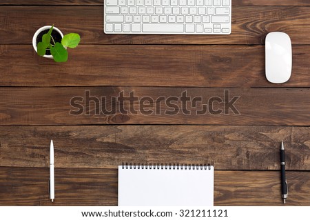 Brown Wooden Desk with Stationery Electronics and Flora\
Natural Wood Background Small Green Plant Computer Mouse and Keyboard Black and White Pens Blank Notepad Top View