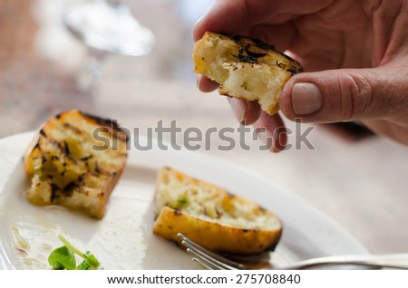 Hand is holding a piece of toasted garlic bread with garlic bread on a plate in the background