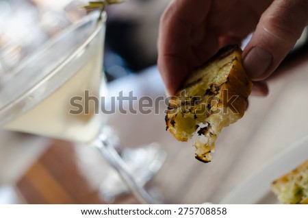 Holding garlic bread between two fingers with martini in the background