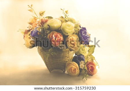 A group of artificial colorful roses put in the bamboo basket under the strong light with the soft shadow on the back wall and hard shadow on the floor, in the blur sweet light vintage tone