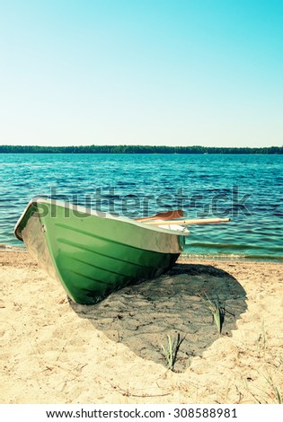 Green rowing boat pulled to the beach in Finland. In the background is the lake. Image includes a effect.