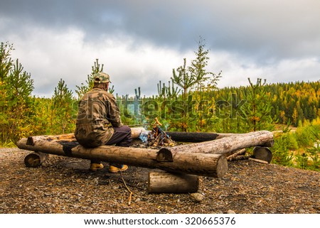 A man warms sausages above the campfire in Finland. The man has a camouflage clothes. In the background is the autumn forest.