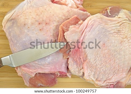 A close view of two turkey thighs and a sharp knife on a wood cutting board.