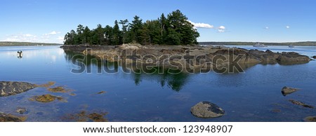 A panoramic view of a small island off the coast of Maine with boats on either side.
