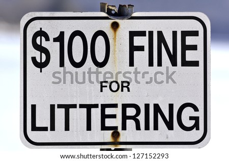 Close view of an old fine for littering sign with bent top and worn metal post outdoors.