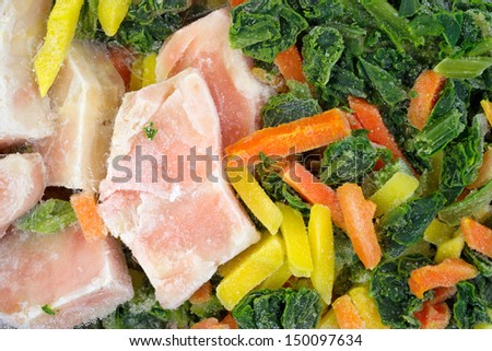 A very close view of frozen salmon with carrots and spinach.