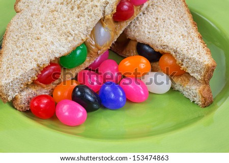 A close view of a peanut butter and jelly bean sandwich on a green plate with extra jelly beans.