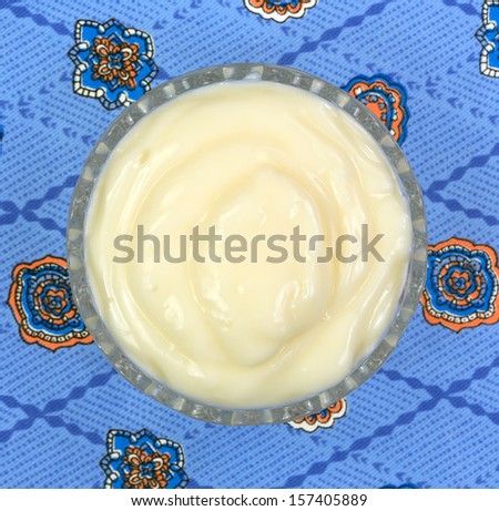 A small glass bowl filled with Boston cream pie flavored yogurt on a colorful blue pattern tablecloth.