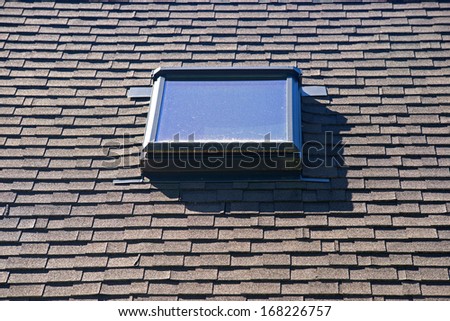 A skylight on an asphalt shingled roof.