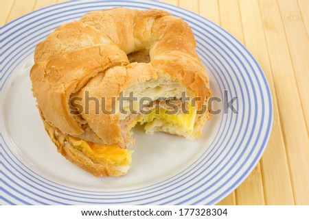 A bitten croissant breakfast sandwich with sausage egg and cheese on a blue striped plate.