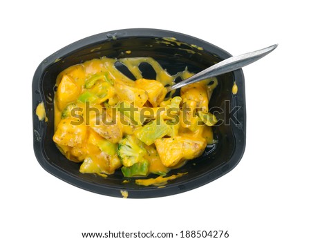 Top view of a TV dinner of potatoes and broccoli in a cheese sauce with a spoon on a white background.