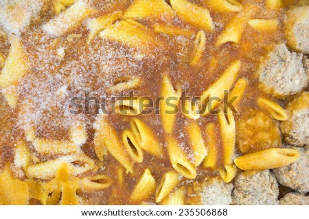 A very close view of a frozen TV dinner of penne pasta in a tomato sauce with meatballs.
