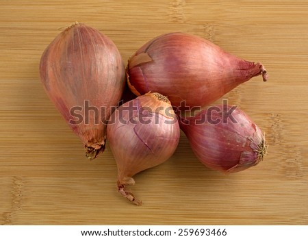 A group of four fresh shallots on a wood cutting board.