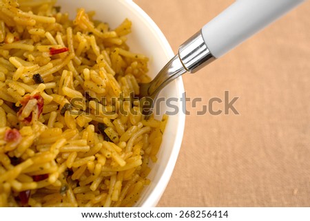 A very close view of a bowl of Mexican rice with a fork on a beige table cloth.