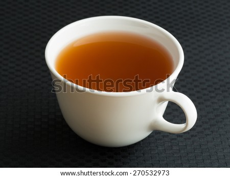 A white cup of passion fruit green tea on a black table cloth.
