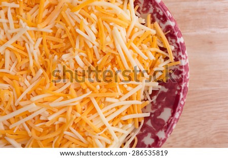 Top close view of a small colorful tray filled with shredded white cheddar, sharp cheddar and mild cheddar cheeses atop a wood table top.