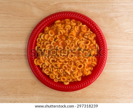Top view of cooked canned round spaghetti pasta in tomato sauce on a red plate illuminated by natural light.