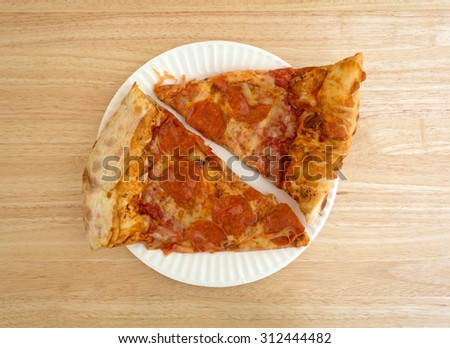 Top view of two slices of freshly baked pepperoni pizza on a white paper plate atop a wood table top illuminated with natural light.