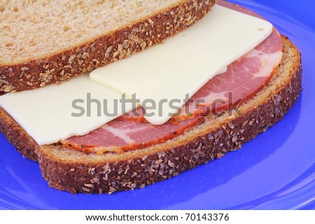 Sandwich with hot capicola and white cheese and wheat bread on blue plate.