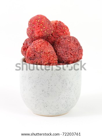 Several freeze dried strawberries in a small dish on a white background.