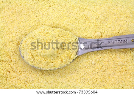 A filled tablespoon atop a layer of stone ground yellow corn meal.