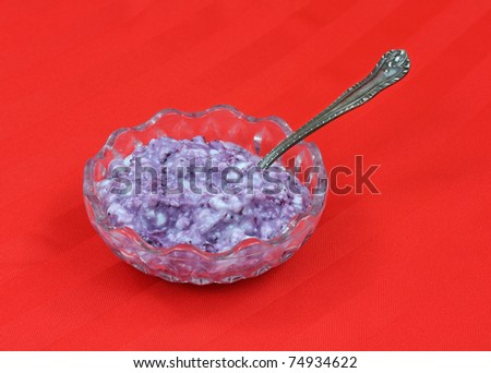 A small serving of cottage cheese with blueberries and spoon in small dish on a red cloth background.