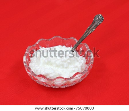 A small serving of cottage cheese with spoon in small dish on a red cloth background.
