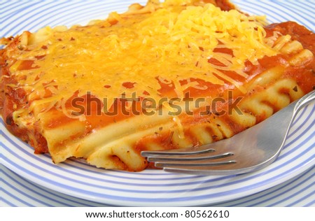 Close view of a small serving of diet lasagna pasta with yellow cheese melted on top on a blue striped plate with fork.