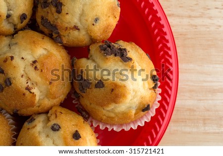 Top close view of small bite size chocolate chip muffins on a red plate atop a wood table top illuminated with natural light.