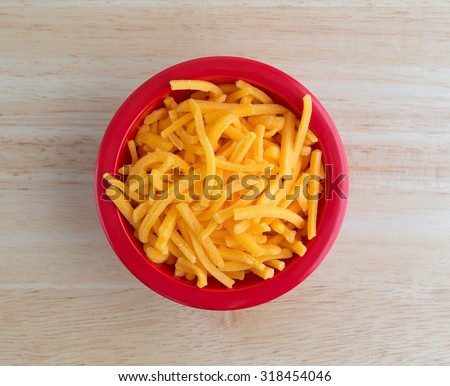 Top view of a bowl of shredded sharp cheddar cheese on a wood table top illuminated with natural light.