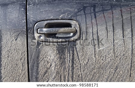 Close view of the door and body panel of a very dirty black car.