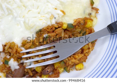 A very close view of microwaved rice and beans with melted cheese and sour cream with fork.