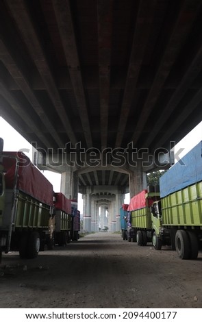 Many green cargo trucks are parked regularly in a large parking area under a big bridge.. Stock foto © 