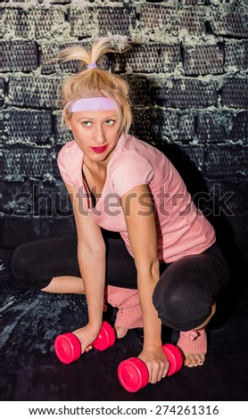 Sexy woman in sportswear, leggings and leg warmers, squatting and lifting pink dumbbells. Concept of modern woman who doesn\'t renounce her femininity and sensuality to keep her fit and her energy
