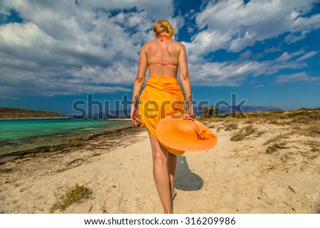 Beautiful woman in orange dress walking on tropical beach. Elafonisos, the Greek version of the Maldives, the island\'s most exotic Mediterranean with turquoise waters, Peloponnese, Greece.