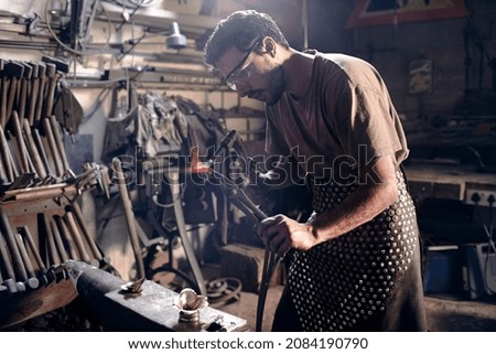 Similar – Image, Stock Photo Focused young blacksmith heating and striking metal on anvil in workshop